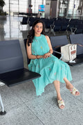 Woman in a teal dress sitting in an airport terminal holding a red cup.